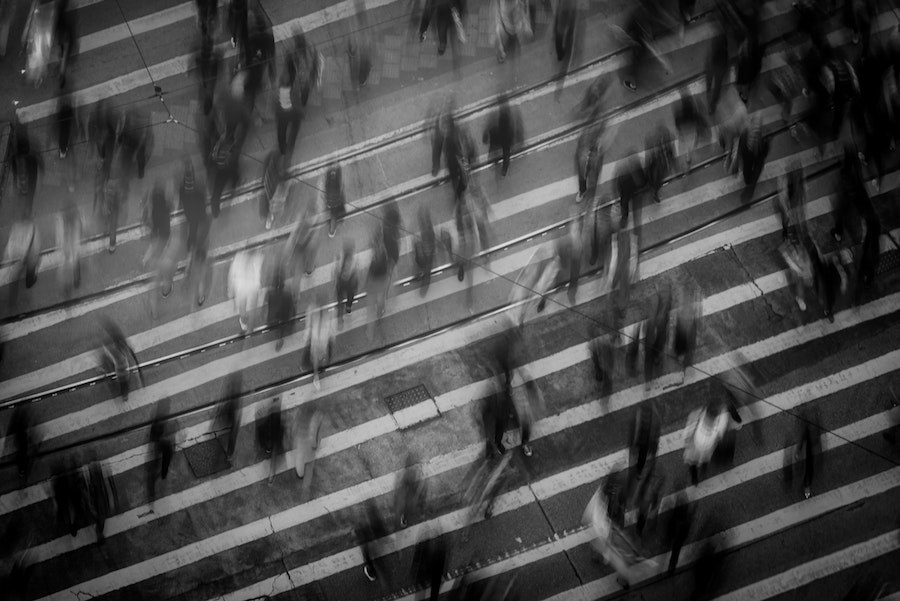A birds eye view in black and white of a road crossing with blurry people walking.